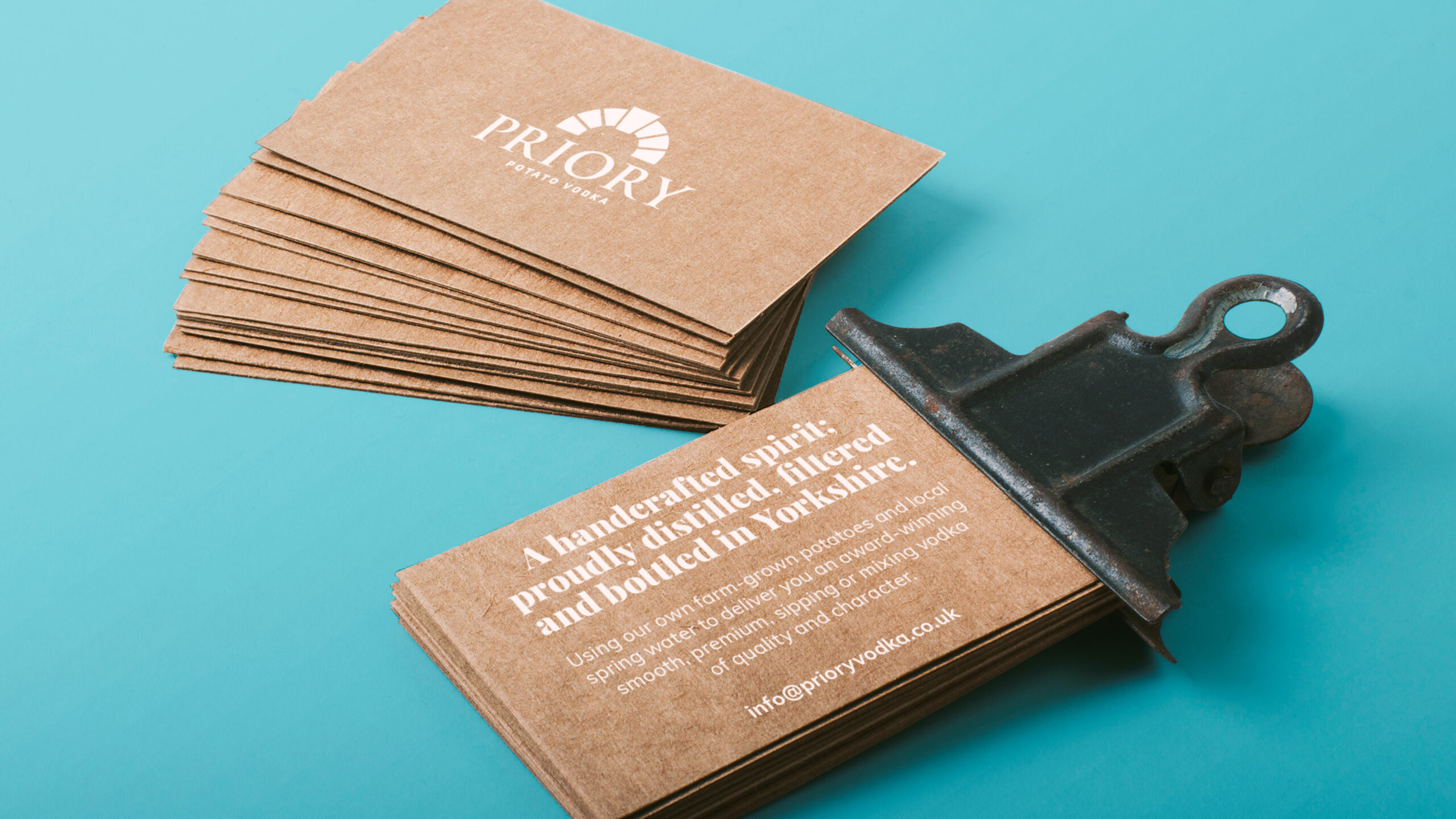 Priory Vodka kraft business cards held in a bulldog clip on blue