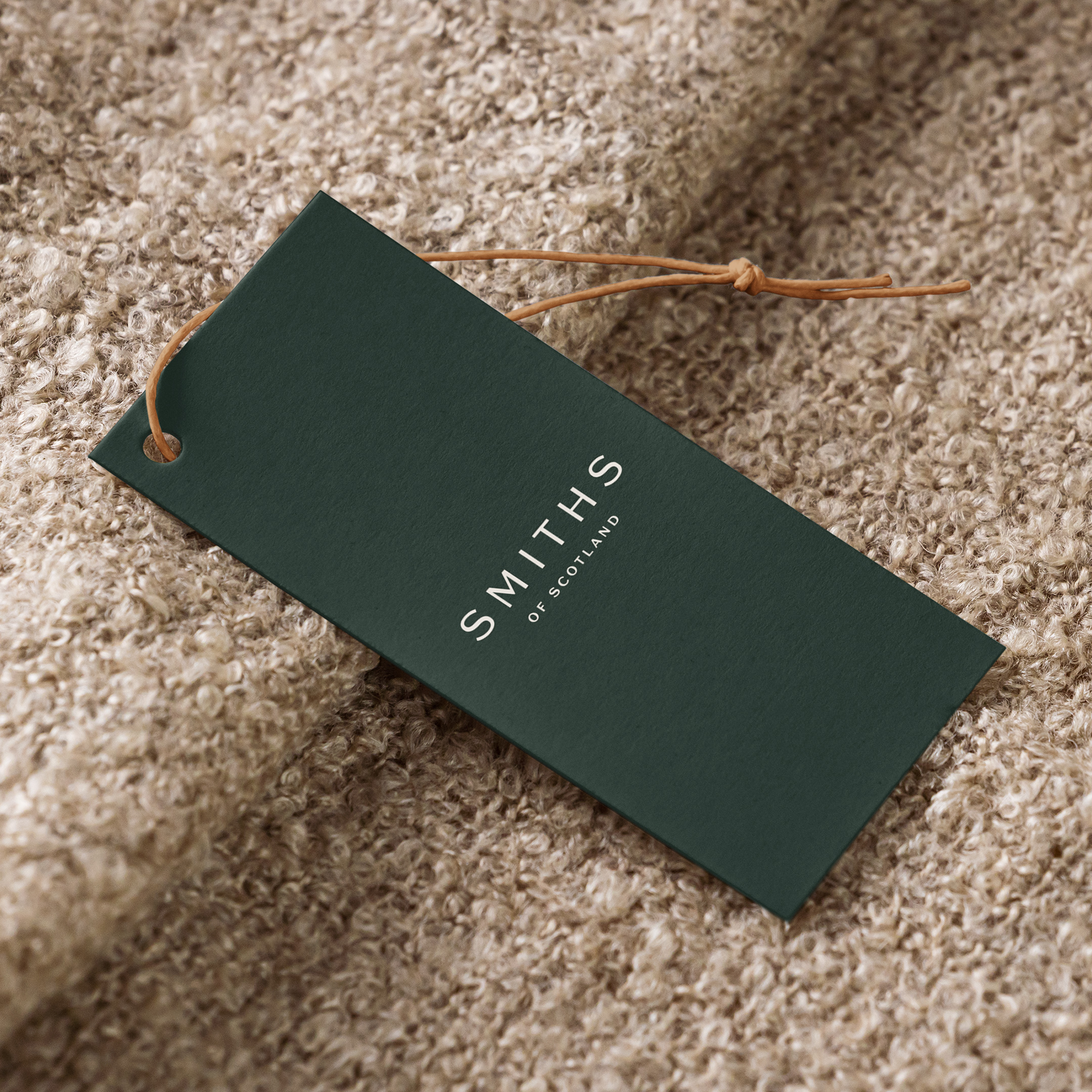Green clothing tag with the Smiths of Scotland wordmark and a leather tie, on knitwear